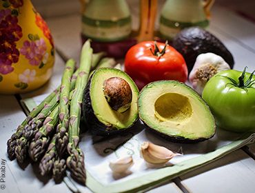 Gesunder Gem&uuml;seteller bestehend aus einer aufgeschnittenen Avocado, zwei ganze Tomaten in rot und gr&uuml;n, gr&uuml;nem Spargel und zwei Knoblauchzehen